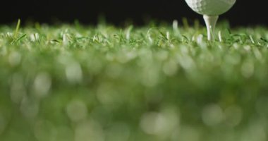 Close up of golf tee and ball on grass and black background, copy space, slow motion. Golf, sport and hobby concept.