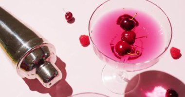 Close up of drinks with cherries and shaker on white background. Cocktail day, party and celebration concept.