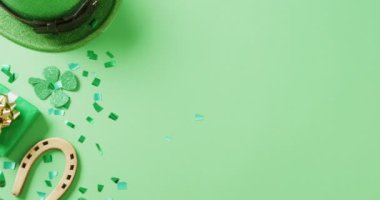 Video of st patrick's green shamrock leaf, horse shoe, hat with copy space on green background. St patrick's day, irish tradition and celebration concept.