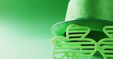Video of st patrick's shamrock leaf glasses and hat with copy space on green to white background. St patrick's day, irish tradition and celebration concept.