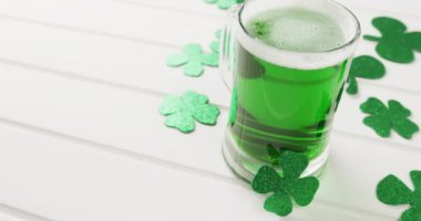 Video of st patrick's green shamrock and green beer with copy space on white background. St patrick's day, irish tradition and celebration concept.