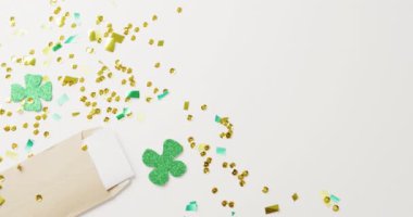 Video of st patrick's green shamrock leaves and sequins with copy space on white background. St patrick's day, irish tradition and celebration concept.