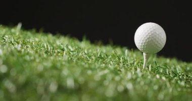 Close up of golf tee and ball on grass and black background, copy space, slow motion. Golf, sport and hobby concept.