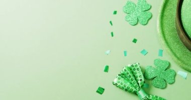 Video of st patrick's green shamrock leaves and hat with copy space on green background. St patrick's day, irish tradition and celebration concept.