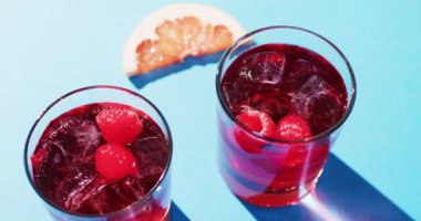 Close up of drinks with raspberries and grapefruit over blue background. Cocktail day, party and celebration concept.