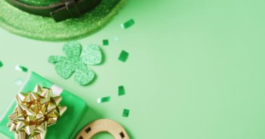 Video of st patrick's green shamrock leaf, present and hat with copy space on green background. St patrick's day, irish tradition and celebration concept.
