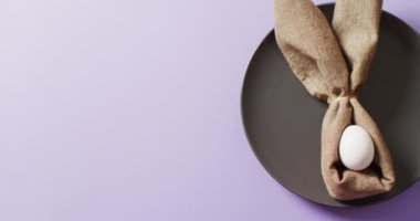 Egg and ribbon in shape of rabbit on plate on purple background with copy space. Easter, tradition and celebration concept.
