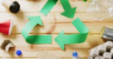 Close up of trash and recycling symbol of green paper arrows on wooden background. Global recycling, ecology and nature concept.
