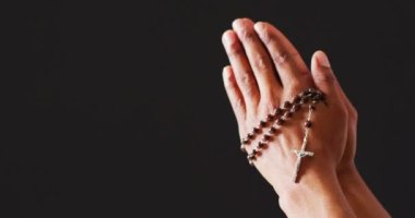 Praying hands with rosary on black background with copy space. Easter, faith, religion, tradition and celebration concept.