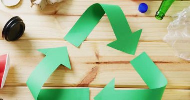 Close up of trash and recycling symbol of green paper arrows on wooden background. Global recycling, ecology and nature concept.