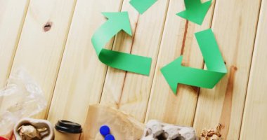 Close up of trash and recycling symbol of green paper arrows on wooden background, with copy space. Global recycling, ecology and nature concept.