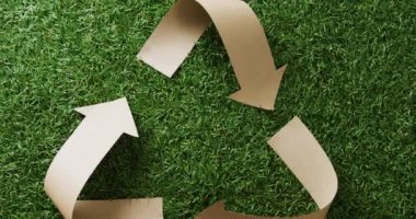 Close up of recycling symbol of paper arrows on grass background, with copy space. Global recycling, ecology and nature concept.