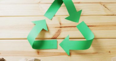 Close up of trash and recycling symbol of green paper arrows on wooden background. Global recycling, ecology and nature concept.