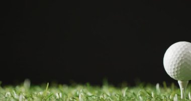 Close up of golf tee and ball on grass and black background, copy space, slow motion. Golf, sport and hobby concept.