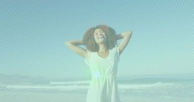 Animation of striped patterns over biracial young woman with arms outstretched spinning at beach. Digital composite, cheerful, afro hair, nature, summer, vacations and enjoyment concept.