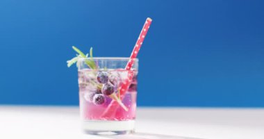 Close up of transparent drink with bluberries on blue background. Cocktail day, party and celebration concept.