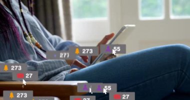 Animation of multiple social media icons over mid section of a woman using digital tablet at home. Social media networking technology concept