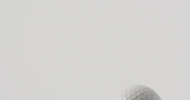 Close up of golf tee and ball on grass and white background, copy space, slow motion. Golf, sport and hobby concept.