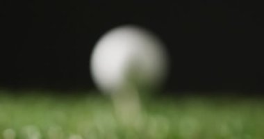 Close up of golf tee and ball on grass and black background, copy space, slow motion. Golf, sport and hobby concept.