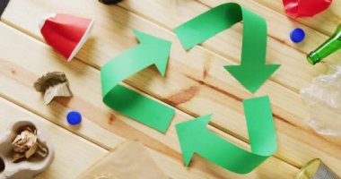 Close up of trash and recycling symbol of green paper arrows on wooden background. Global recycling, ecology and nature concept.