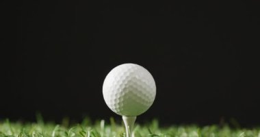 Close up of golf tee and ball on grass and black background, copy space, slow motion. Golf, sport and hobby concept.