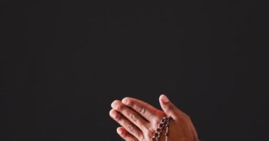 Praying hands with rosary on black background with copy space. Easter, faith, religion, tradition and celebration concept.