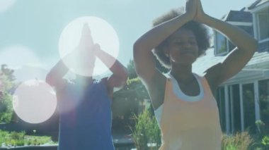 Animation of light spots over african american couple doing yoga, meditating, slow motion. Sport, fitness and healthcare concept digitally generated video.