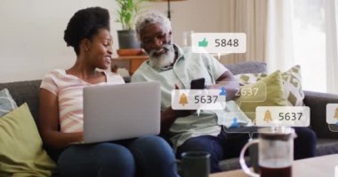 Animation of social media icons and numbers over african american man and woman with laptop. Global social media, networks, computing and data processing concept digitally generated video.