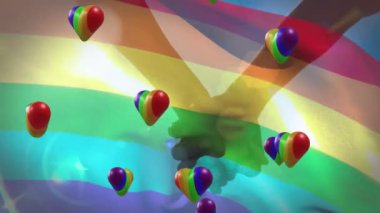 Animation of rainbow hearts and flag over people holding hands. Valentine's day, love and celebration concept digitally generated video.