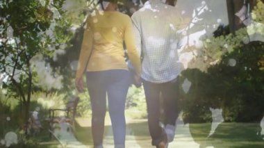 Animation of leaves over african american couple walking in garden. Gardening, lifestyle and nature concept digitally generated video.