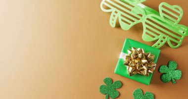 Video of saint patricks day green shamrock, present and glasses with copy space on orange background. Saint patricks day, irish tradition and celebration concept.