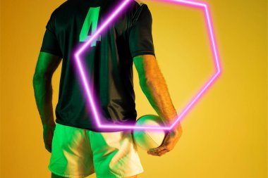Illuminated hexagon over rear view of caucasian male player with rugby ball on yellow background. Copy space, composite, sport, competition, shape, playing, match, hand and abstract concept.