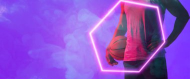 Midsection of biracial basketball player with ball standing by hexagon over smoky background. Blue, composite, copy space, hand, sport, competition, illustration, illuminated, shape and abstract.
