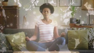Animation of leaves and light spots over african american woman meditating, slow motion. Sport, fitness and healthcare concept digitally generated video.