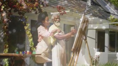 Animation of light spots over african american couple painting on easel in garden. Art, hobby and nature concept digitally generated video