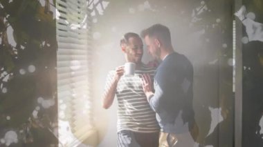 Animation of leaves over diverse male couple embracing and drinking coffee. Valentine's day, love and celebration concept digitally generated video.