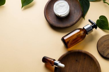 Image of glass bottles with pumps, cream tub on wooden plates and copy space on yellow background. Plastic free beauty, health and beauty, sustainability concept.