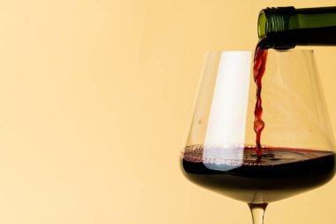 Bottle of red wine and glass on yellow background, with copy space. Wine week, drink and celebration concept.
