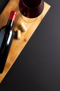 Bottle of red wine, glass and corks on black background, with copy space. Wine week, drink and celebration concept.