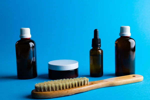 Image of glass bottles, brush and cream tub and copy space on blue background. Plastic free beauty, health and beauty, sustainability concept.