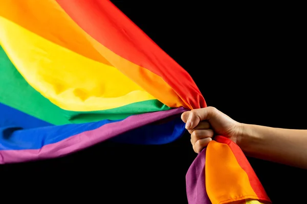 Hand holding rainbow coloured flag with copy space on black background. Pride month, equality, lgbt and human rights concept.