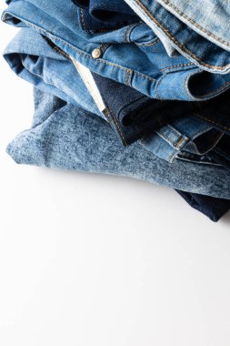 Vertical image of diverse folded jeans lying in stack on white background. Clothes, fashion, design, fabrics, materials and shopping concept.