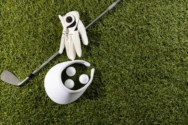 White visor, glove, three golf balls and golf club on grass with copy space. Golf, sports and competition concept.