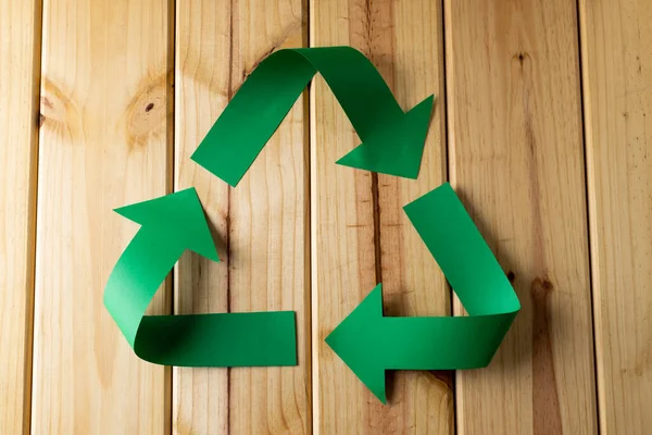 Close up of recycling symbol of paper green arrows on wooden background with copy space. Global ecology and recycling concept.