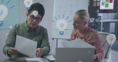 Animation of digital light bulb icons over diverse business people in office. Global business, finances, computing and data processing concept digitally generated video.