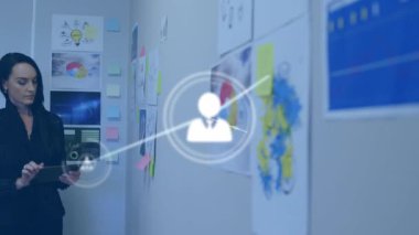 Animation of connected icons over caucasian businesswoman looking at reports and using tablet. Digital composite, multiple exposure, communication, office and technology concept.