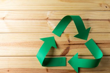Close up of recycling symbol of paper green arrows on wooden background with copy space. Global ecology and recycling concept.