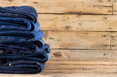 Diverse folded jeans in stack over wooden background. Clothes, fashion, design, fabrics, materials and shopping concept.