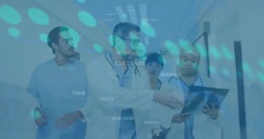 Animation of financial graphs and data over diverse female and male doctors walking with x ray photo. Medicine, health care and finance concept digitally generated video.