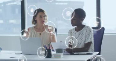 Animation of digital icons over diverse business women in office. Global business, finances, computing and data processing concept digitally generated video.